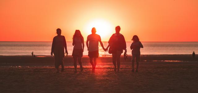 silhouette photo of five person walking on seashore during golden hour by Kevin Delvecchio courtesy of Unsplash.